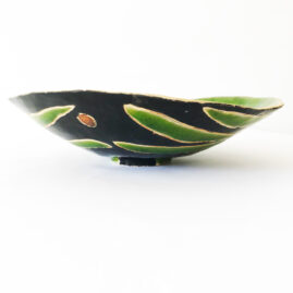 Ceramic flat bowl in blue with green leafs taken from the side